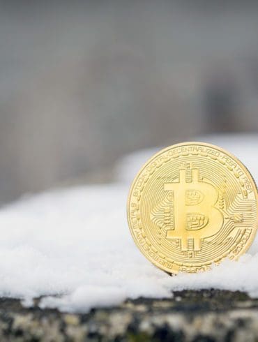 A gold Bitcoin placed in snow on concrete. Isolated scene of cryptocurrency in snow