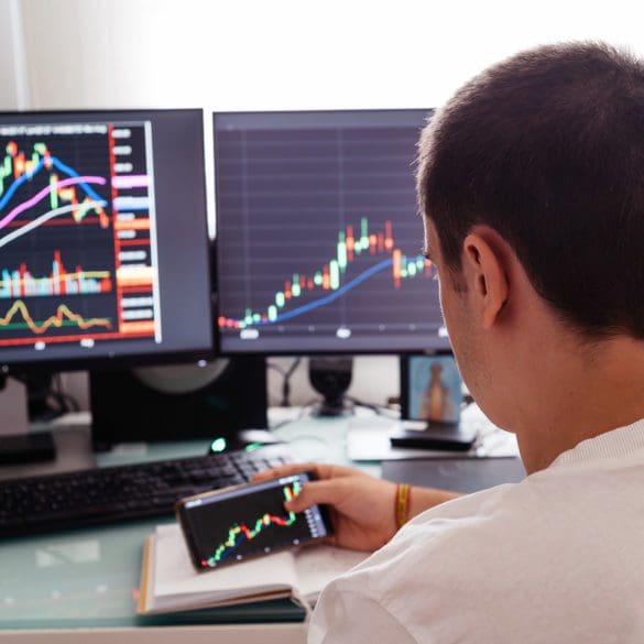 Busy working day at home. Side view of successful young trader in casual wear working with charts and market reports on computer screens in his home.