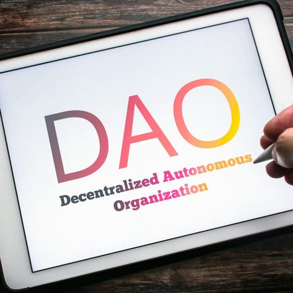 The sign of DAO (Decentralized Autonomous Organization), an organization represented by rules encoded as a transparent computer program, on tablet on wooden table. Man hand holding wireless stylus