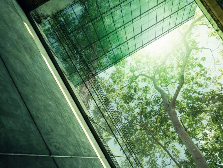 Sustainble green building. Eco-friendly building in modern city. Sustainable glass office building with tree for reducing carbon dioxide. Office with green environment. Corporate building reduce CO2.